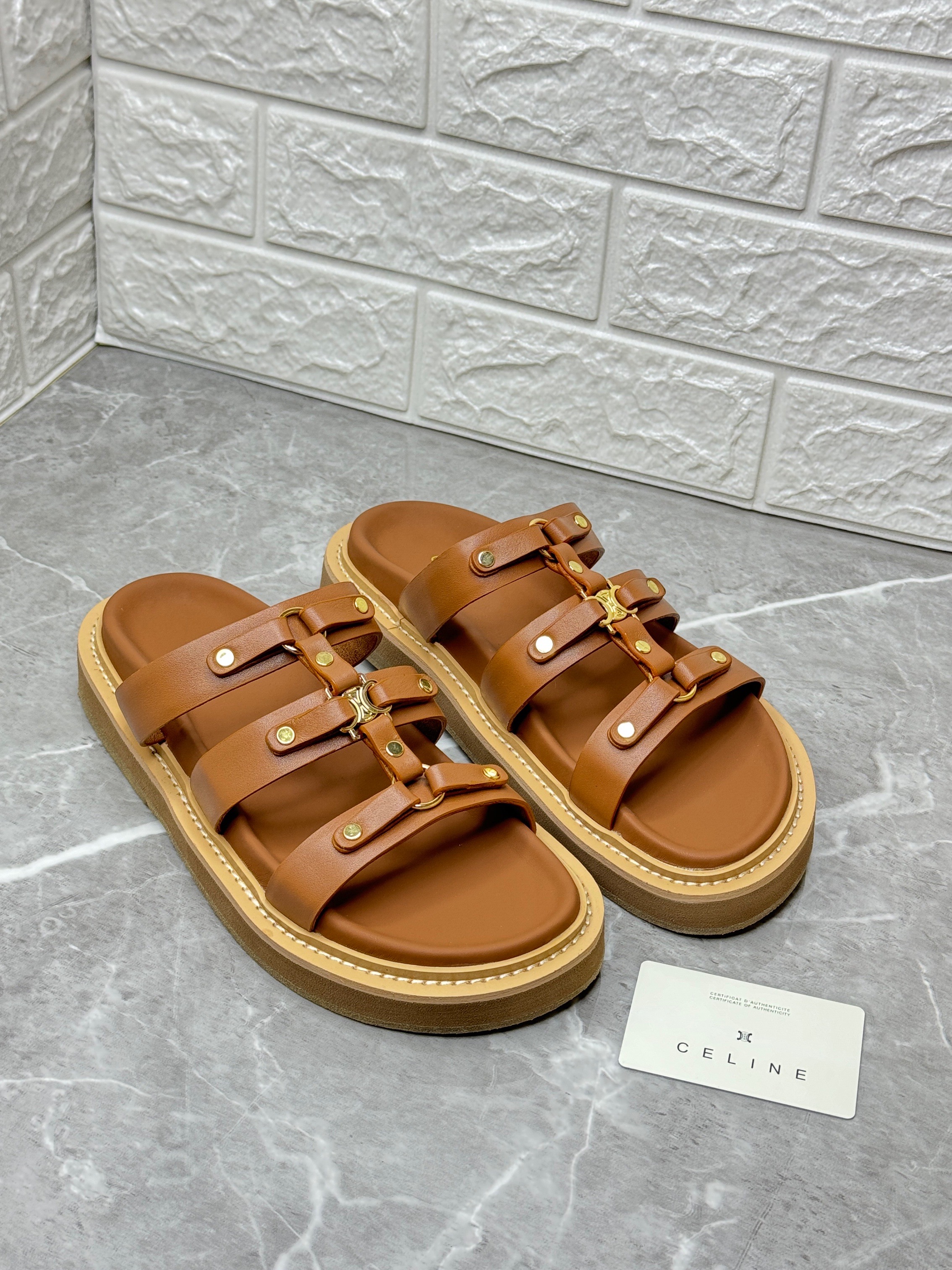 Celine Tippi slide sandals in brown or tan calfskin leather, featuring Triomphe hardware and a rubber outsole with a foam insert for comfort. image 1