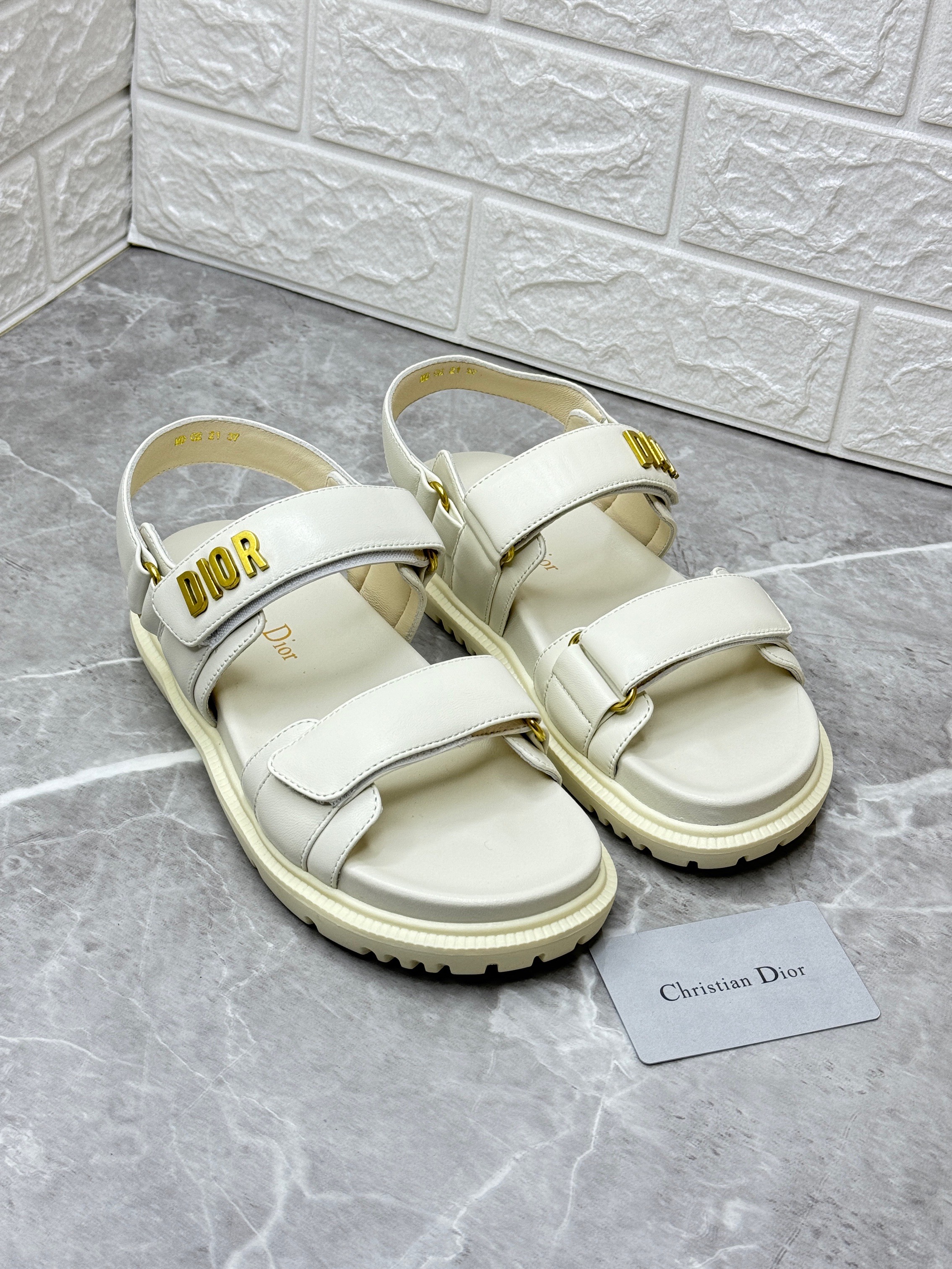 Dior Dioract sandals in powder beige lambskin with gold-finish metal "DIOR" signatures. The sandals feature two adjustable self-fastening straps and an anatomically shaped leather insole for comfort. image 1