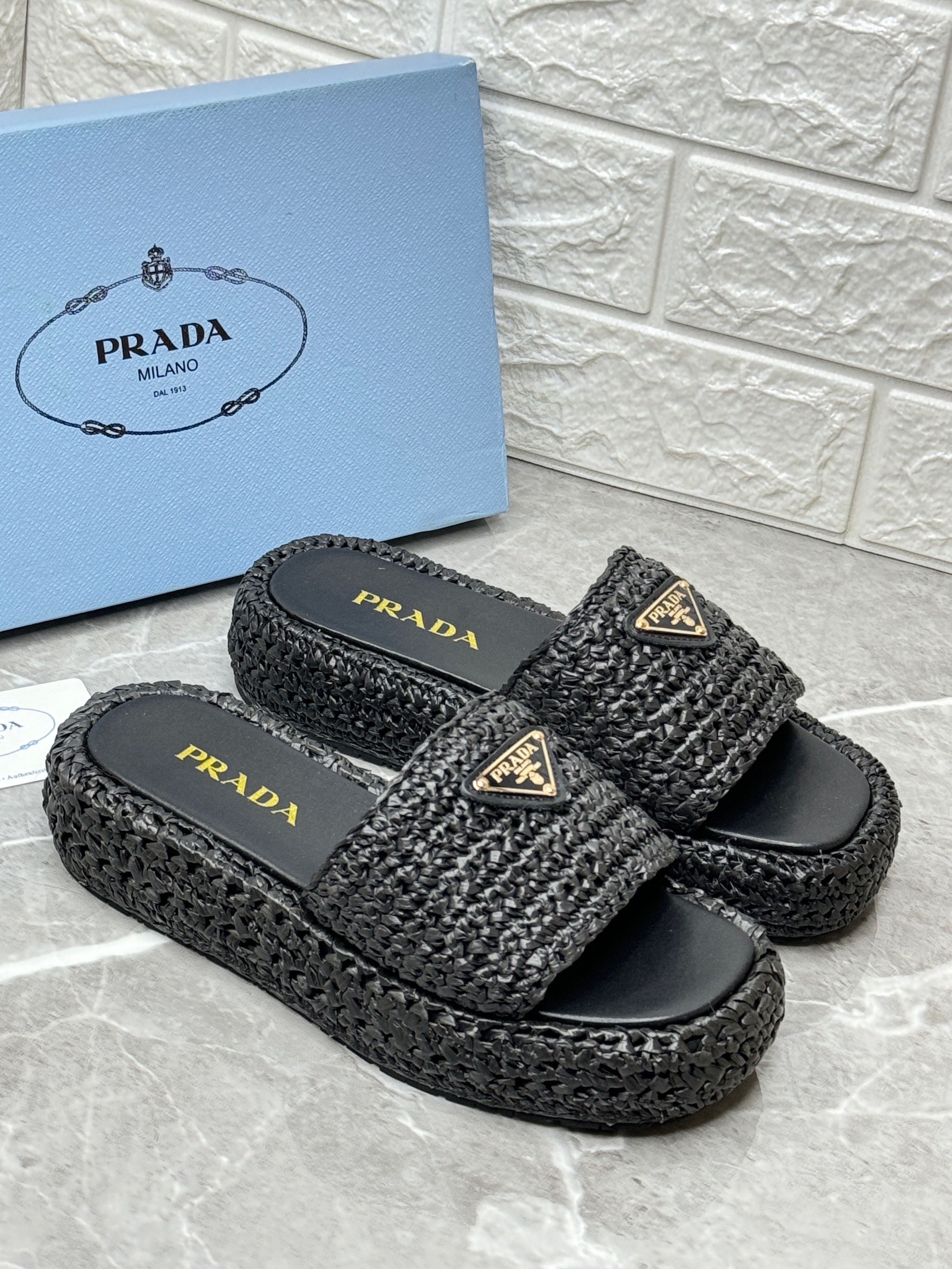 Prada black crochet flatform slides made from raffia-effect yarn, featuring an enameled metal triangle logo and a 35mm monoblock rubber sole. image 1