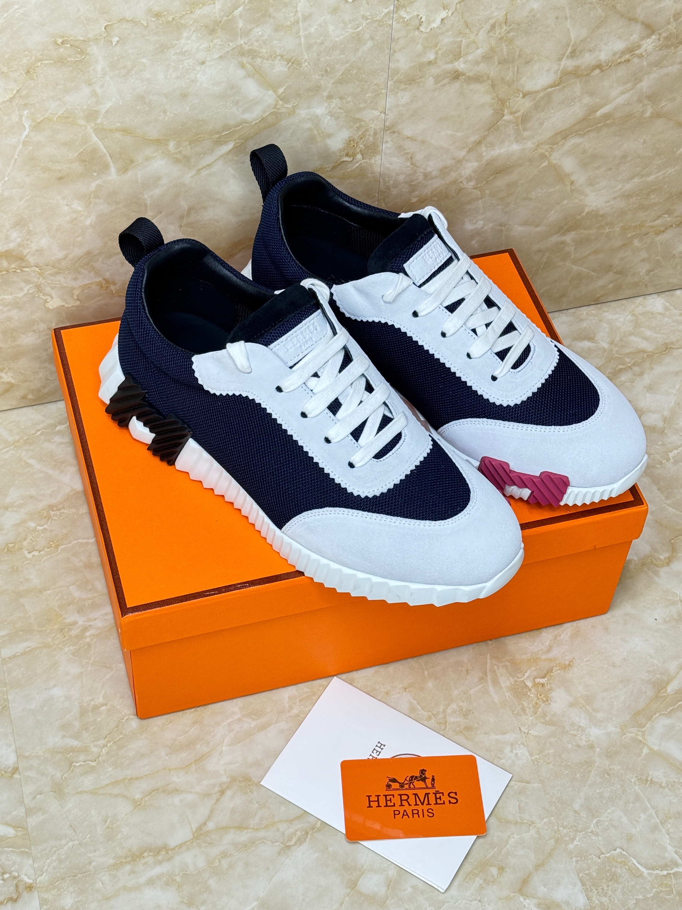 Herm?s Bouncing sneakers in technical mesh and suede goatskin, featuring a black and white upper with a light rubber sole that has a pink/orange accent on the bottom. image 1