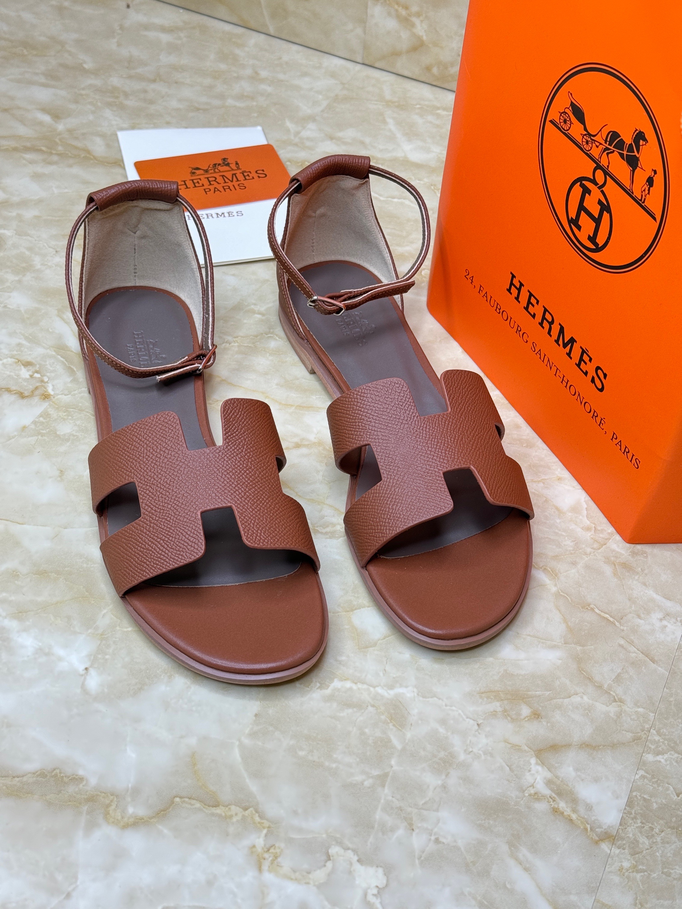 Herm?s Santorini leather sandals in a dark red or brown color, featuring the iconic "H" cut-out detail and an adjustable ankle strap. image 1