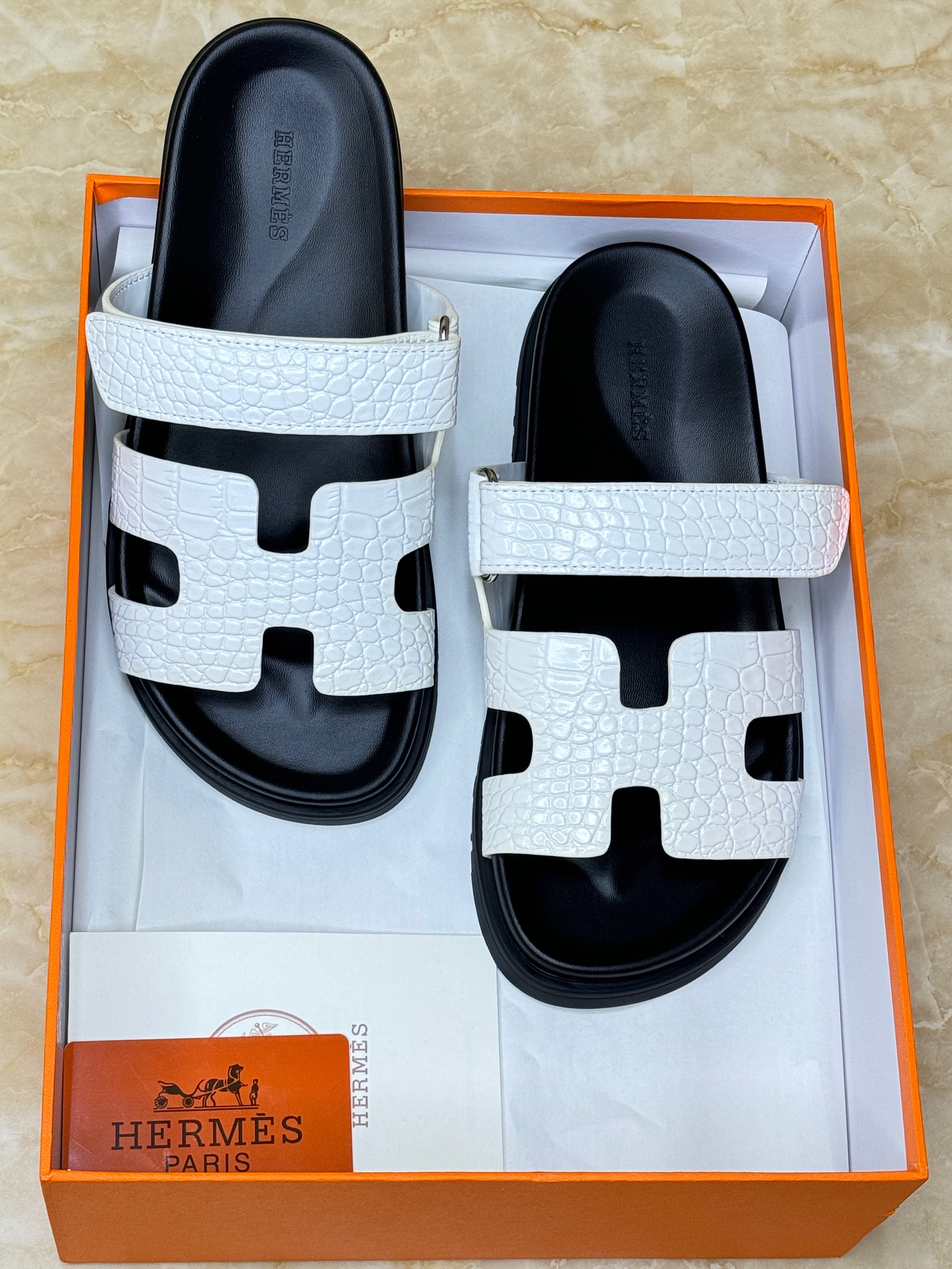 Herm?s Chypre sandals with an adjustable strap and the signature "H" cut-out, crafted from white crocodile-embossed leather and featuring an anatomical black rubber sole. image 1