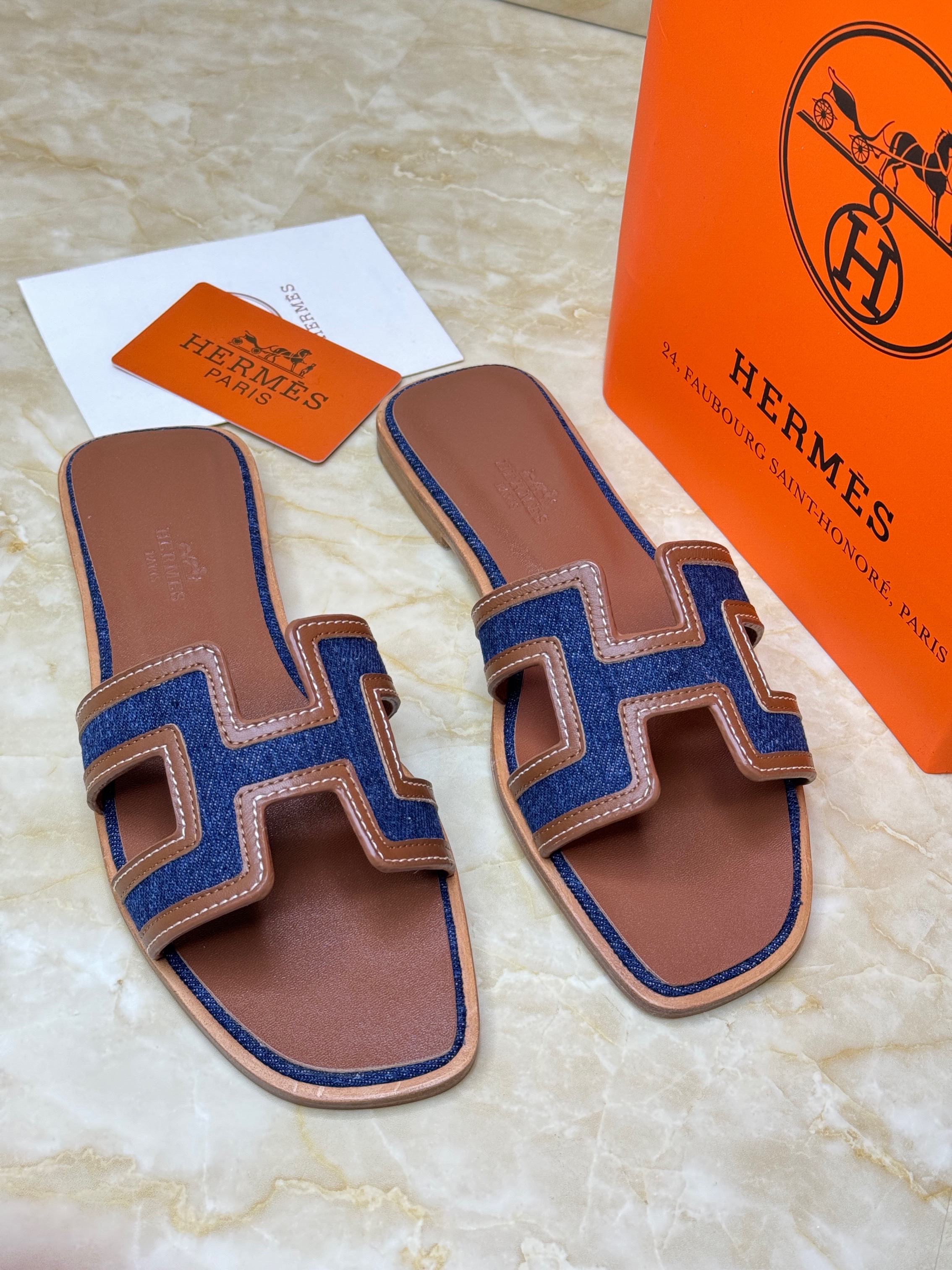 Herm?s Oran sandals with the iconic "H" cut-out, featuring a brown leather sole and a strap crafted from blue denim and tan calfskin leather. image 1