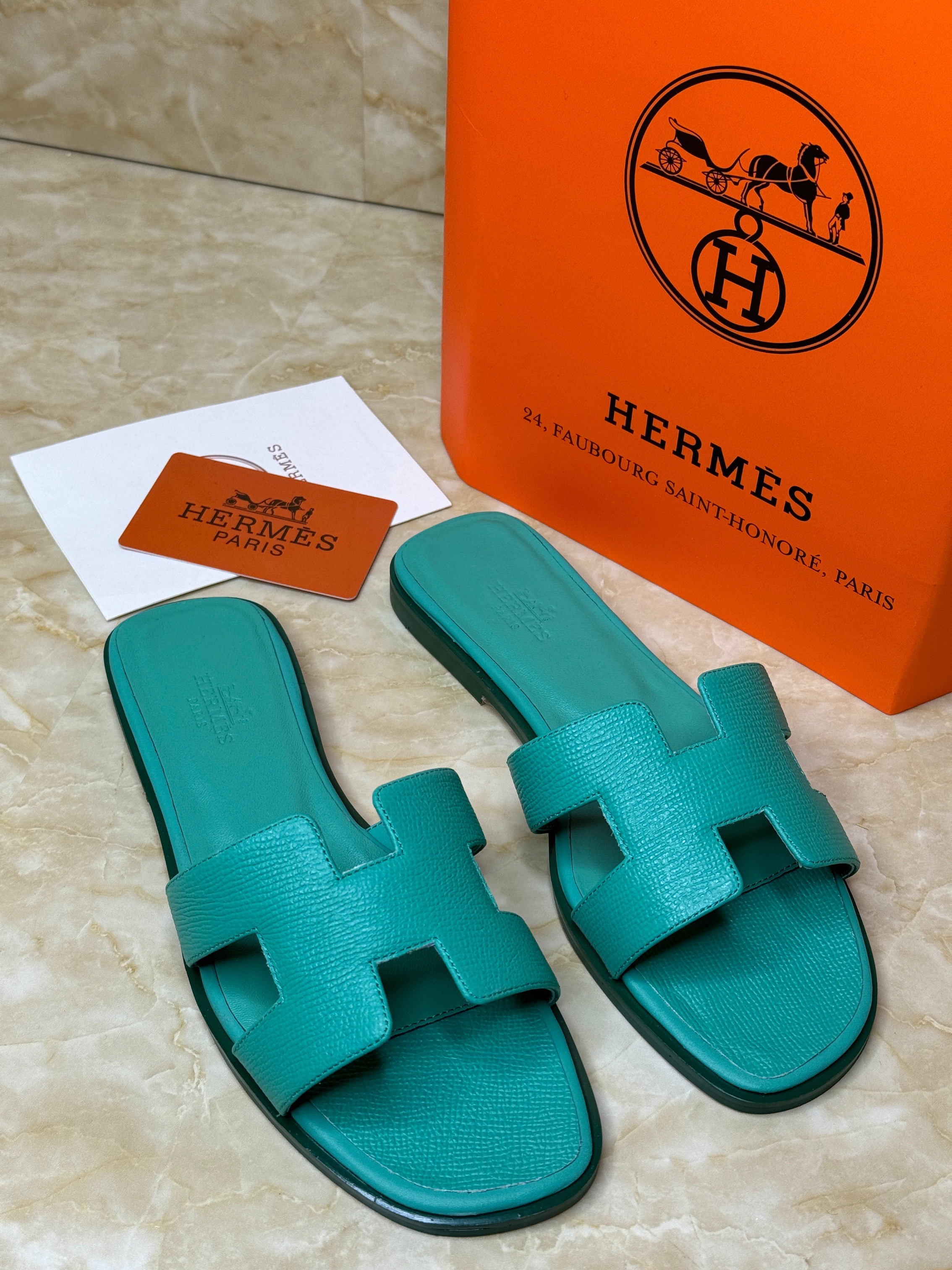 Herm?s Oran sandals in calfskin leather with an iconic "H" cut-out design, shown here in a teal or blue-green color. image 1