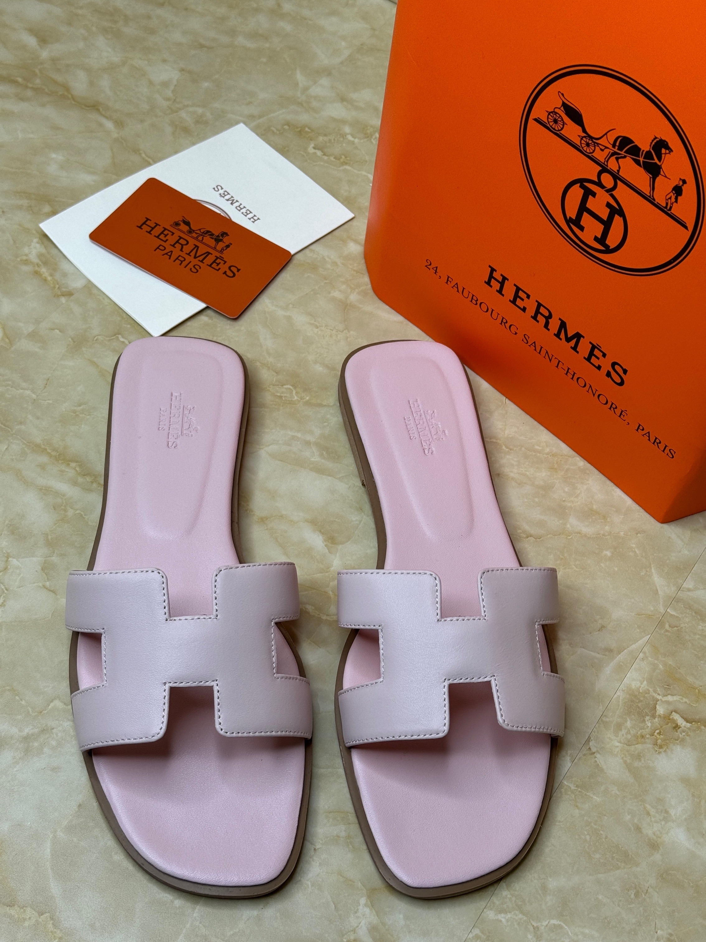 Herm?s Oran sandals in calfskin leather, featuring the brand's iconic "H" cut-out strap design. They are a light pink color, likely known as Rose Cancan. image 1
